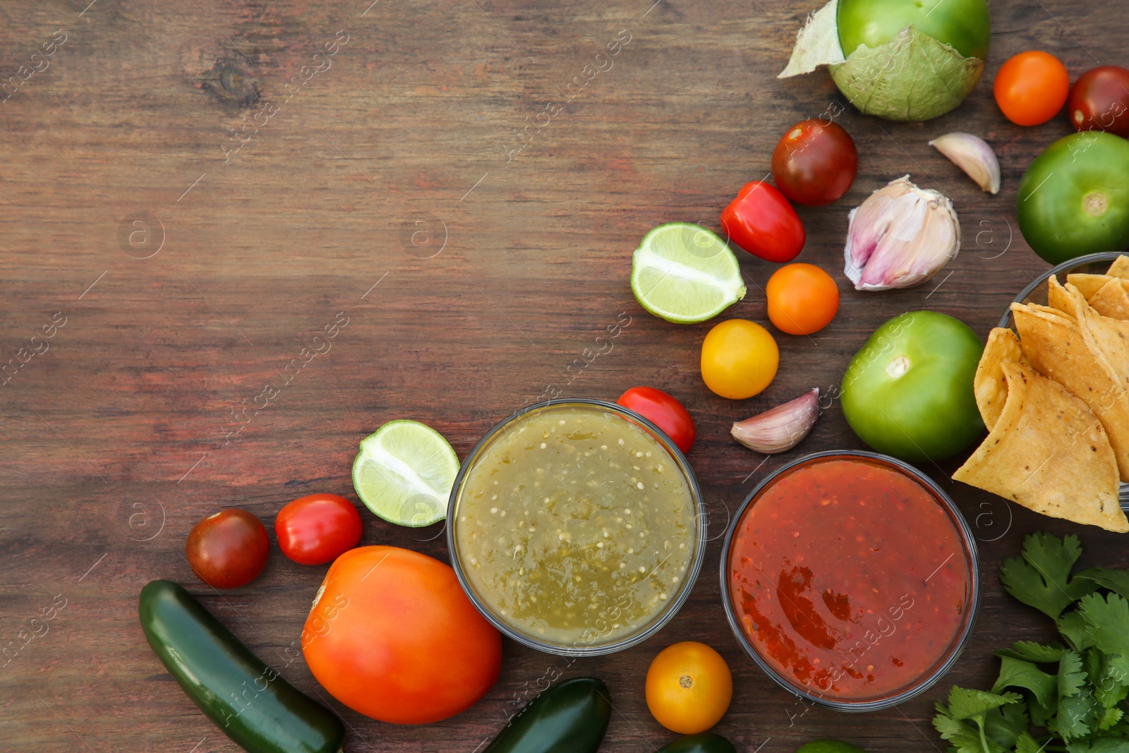 Photo of Flat lay composition of tasty salsa sauces and different ingredients on wooden table. Space for text