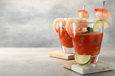 Tasty shrimp cocktail with sauce in glasses and lime on light grey table, space for text