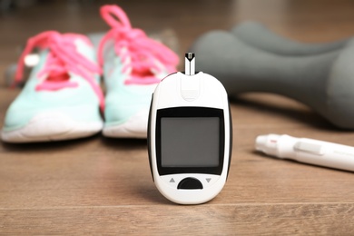 Photo of Digital glucometer, dumbbells and sneakers on wooden background. Diabetes concept