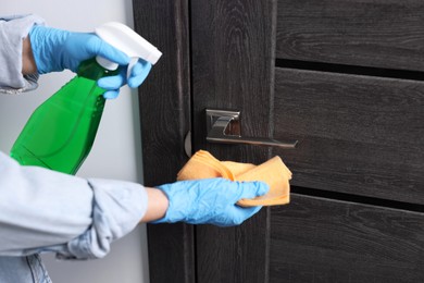 Photo of Woman cleaning door handle with detergent and rag indoors, closeup