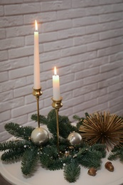 Christmas composition with burning candles on white table near brick wall