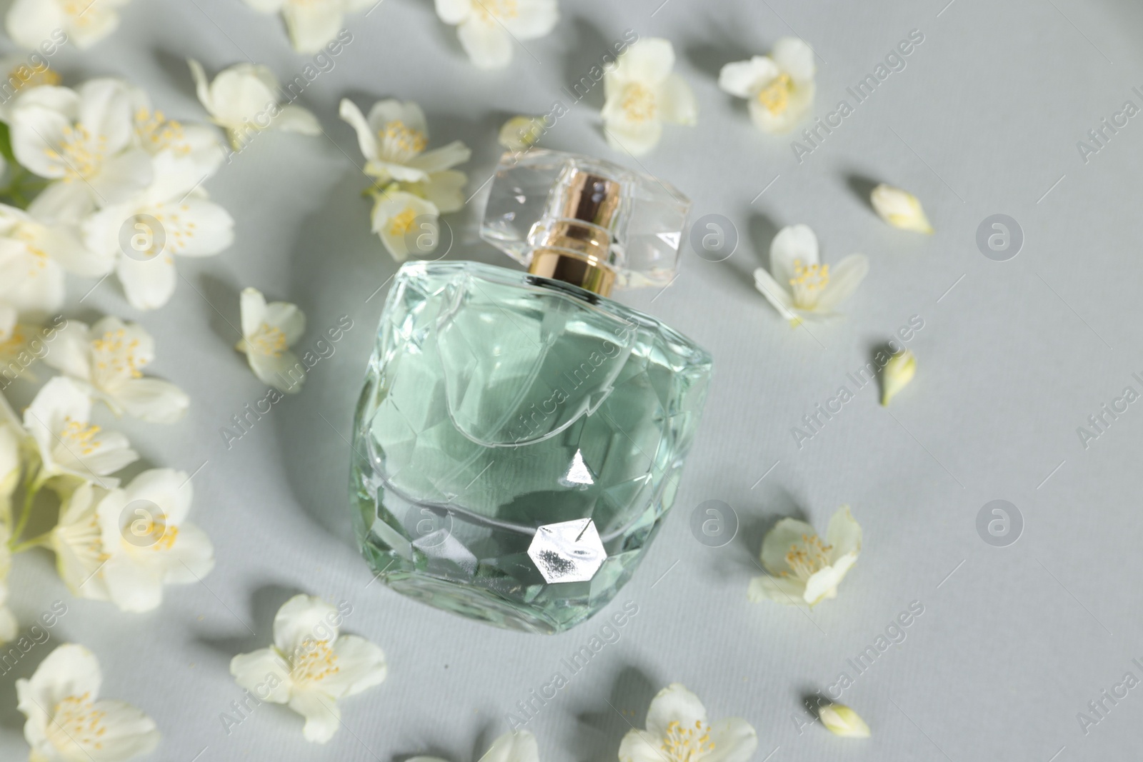 Photo of Aromatic perfume in bottle and beautiful jasmine flowers on grey background, flat lay