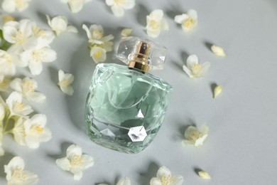 Aromatic perfume in bottle and beautiful jasmine flowers on grey background, flat lay