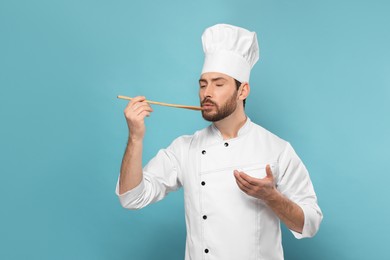 Photo of Mature male chef with spoon tasting dish on light blue background, space for text