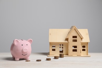 Photo of Piggy bank, little house model and stacks of coins on white wooden table