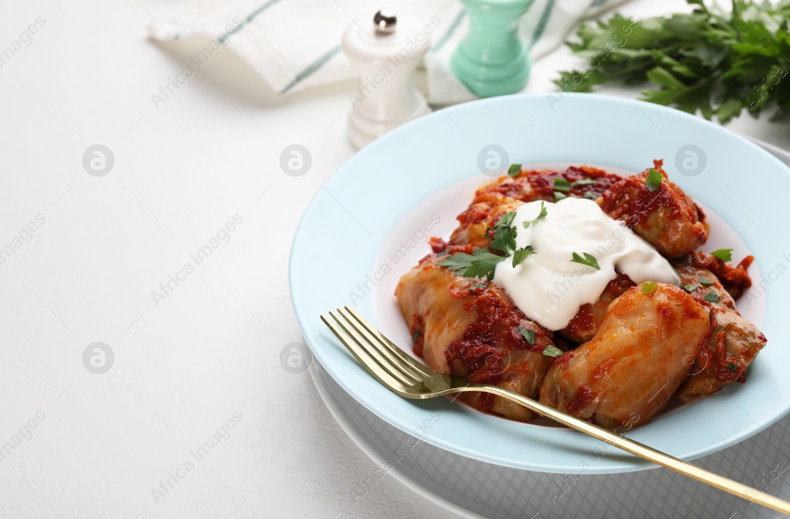 Photo of Delicious stuffed cabbage rolls served with sour cream on white table, closeup. Space for text