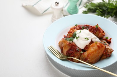 Delicious stuffed cabbage rolls served with sour cream on white table, closeup. Space for text