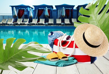 Image of Stylish bag with beach accessories on white wooden surface near outdoor swimming pool