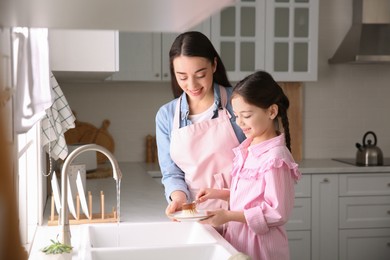 Mother and daughter washing dishes together in kitchen