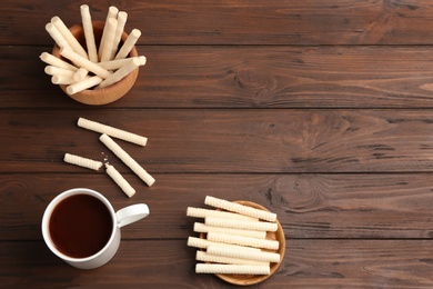 Flat lay composition with wafer rolls and cup of cocoa on wooden background, space for text