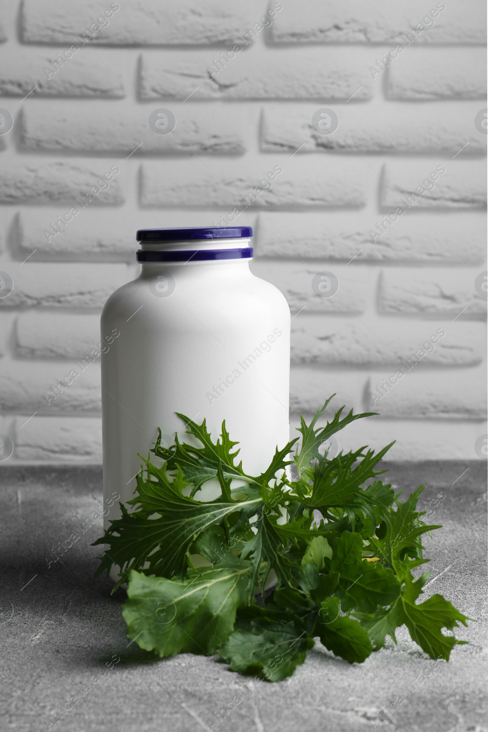 Photo of White medical bottle and arugula on light gray textured table