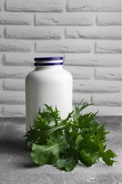 Photo of White medical bottle and arugula on light gray textured table