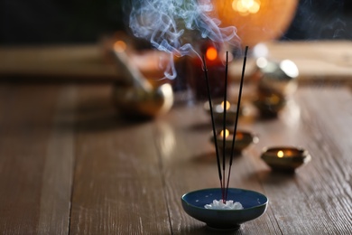 Photo of Incense sticks smoldering on wooden table in room. Space for text