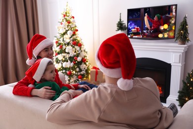 Family watching festive movie on TV in room decorated for Christmas