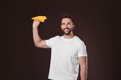 Handsome man playing with paper plane on brown background