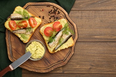 Photo of Delicious sandwiches with sprats, tomatoes, dill and avocado puree served on wooden table, top view. Space for text
