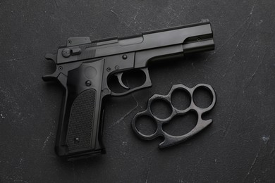 Photo of Brass knuckles and gun on black stone background, flat lay