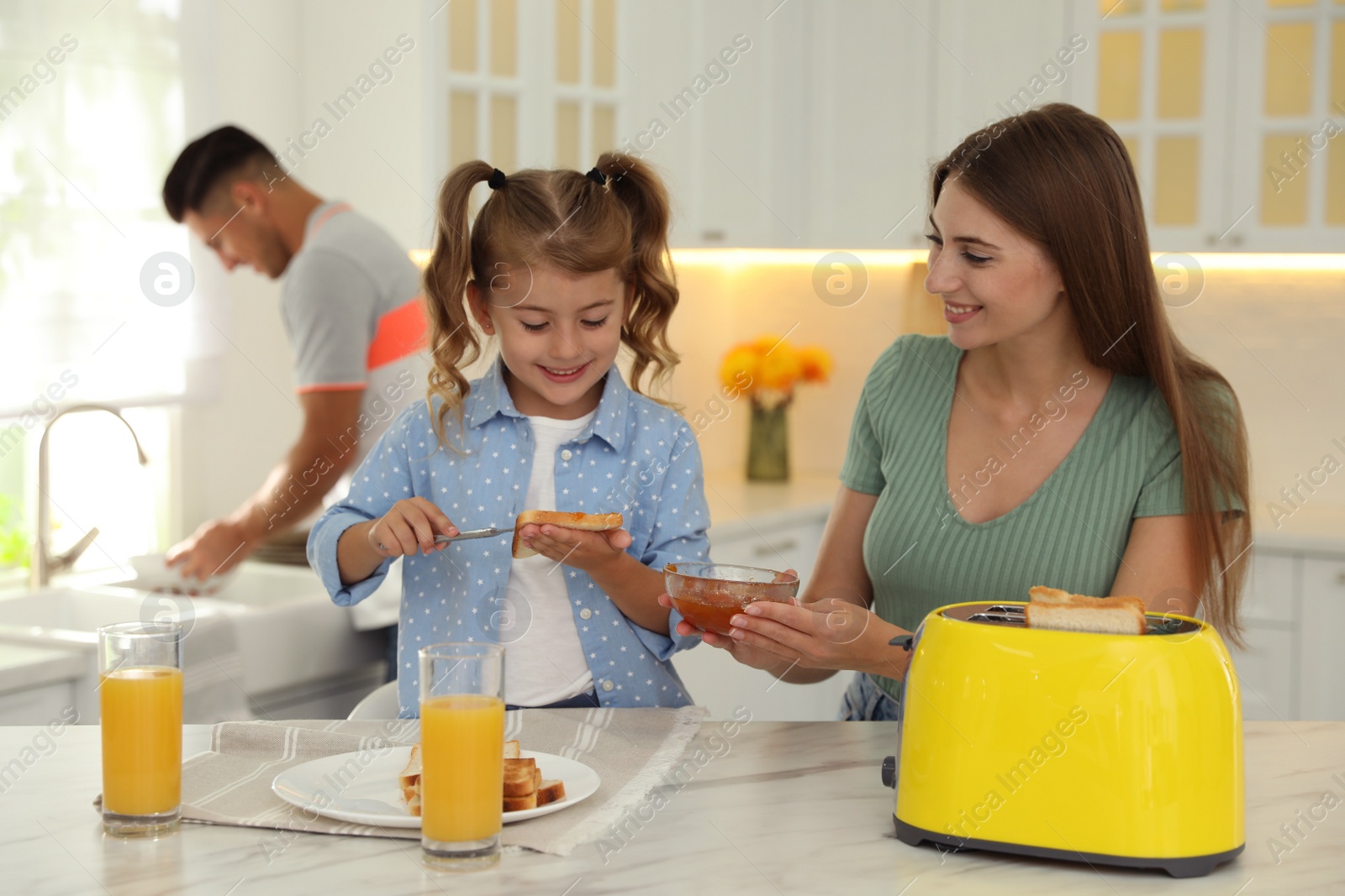 Photo of Happy family having breakfast with toasted bread at table in kitchen