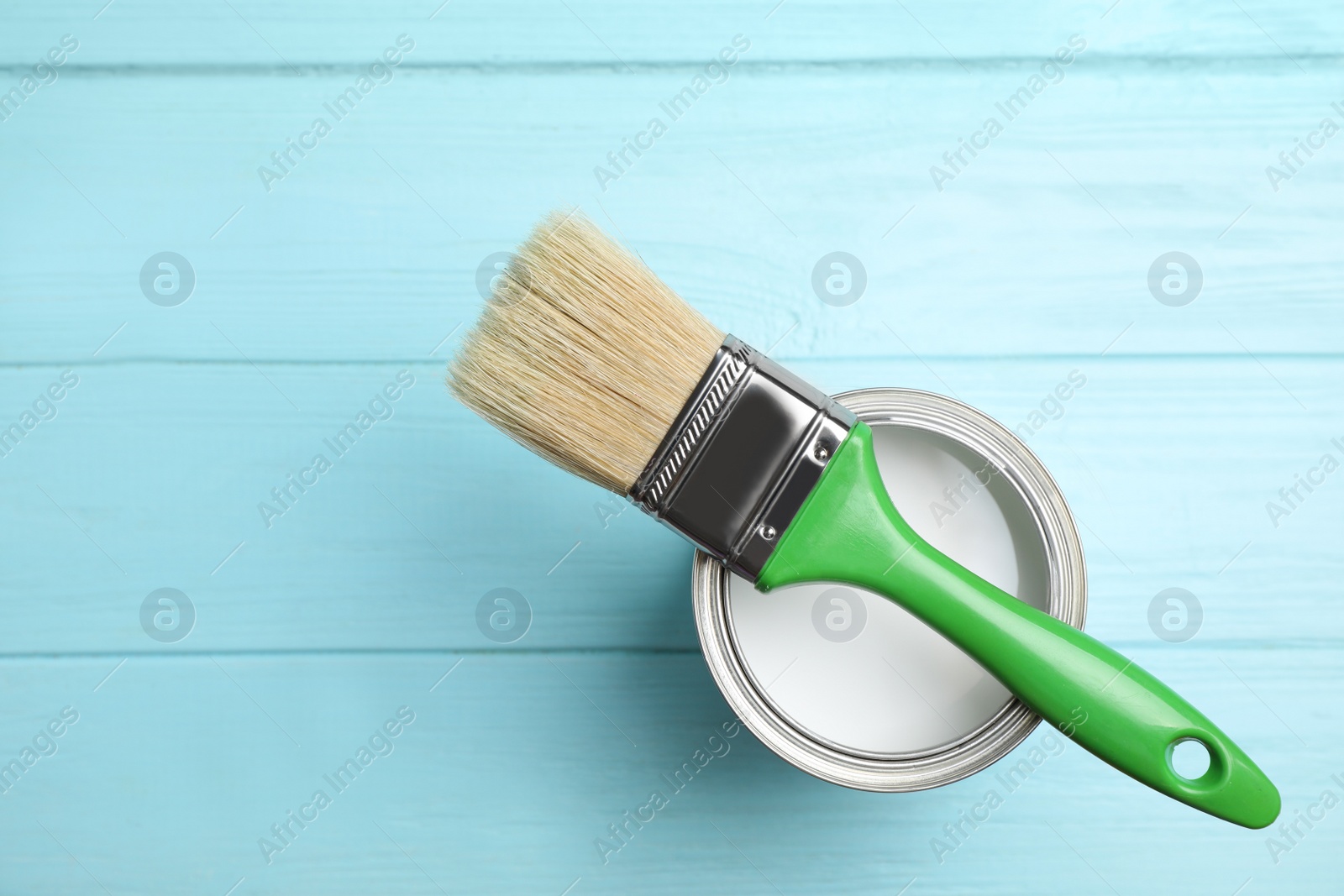 Photo of Open can with white paint and brush on blue wooden table, top view. Space for text