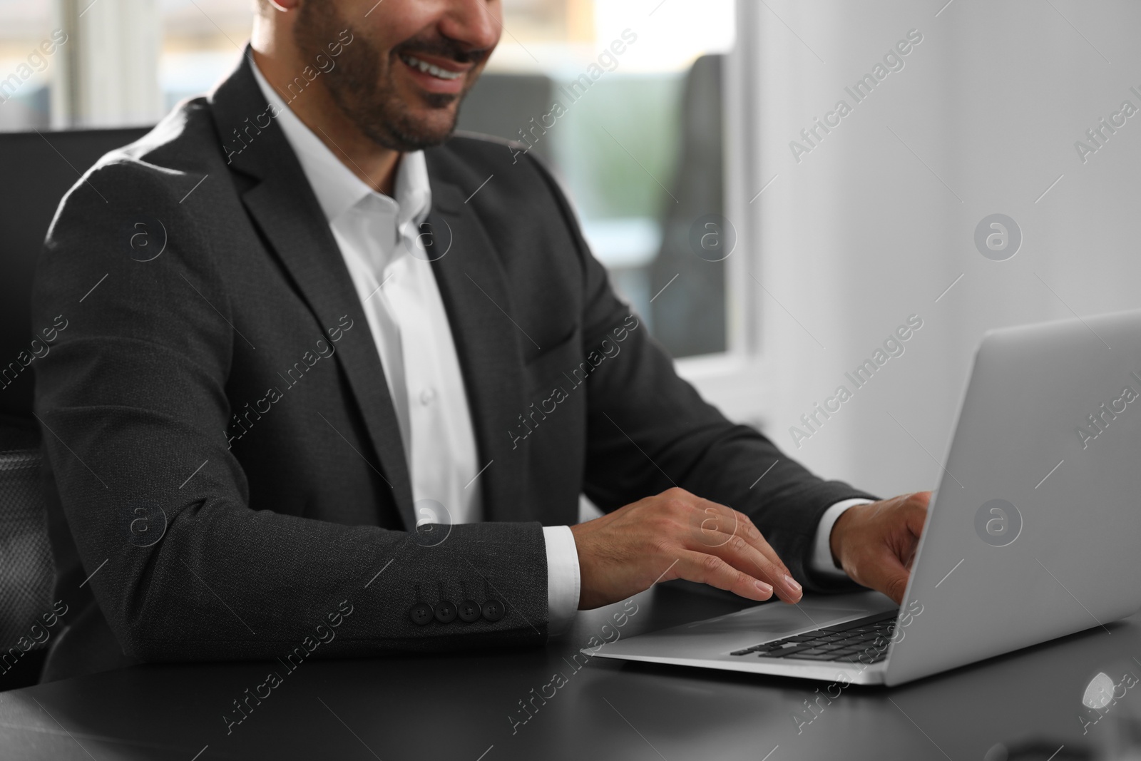 Photo of Man using modern laptop at black desk in office, closeup