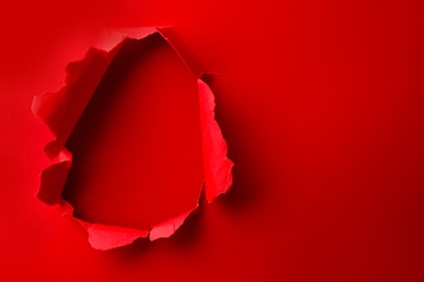 Photo of Hole in red paper on color background, space for text