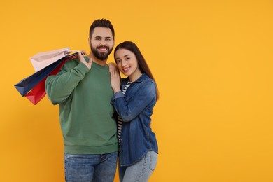 Photo of Happy couple with shopping bags on orange background. Space for text