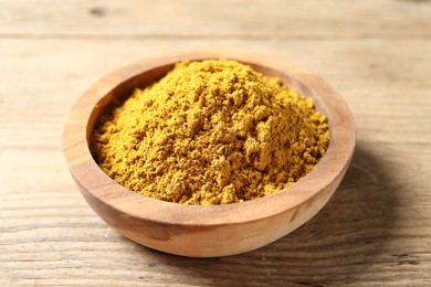 Photo of Dry curry powder in bowl on wooden table, closeup