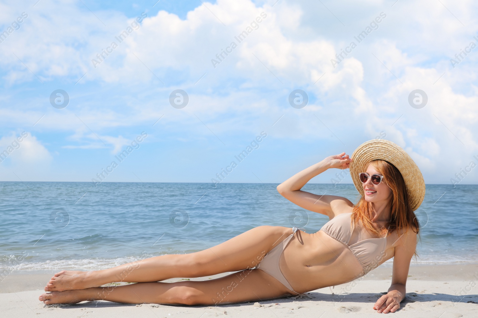 Photo of Attractive woman with perfect body in bikini lying on sandy beach near sea