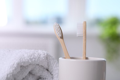 Photo of Bamboo toothbrushes in holder and towel on blurred background, closeup