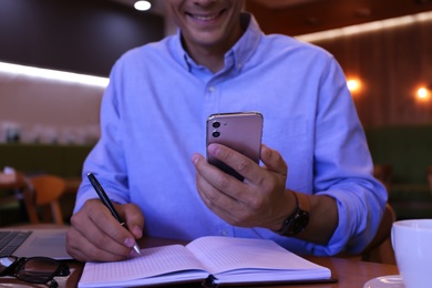 Businessman with smartphone working in cafe, closeup