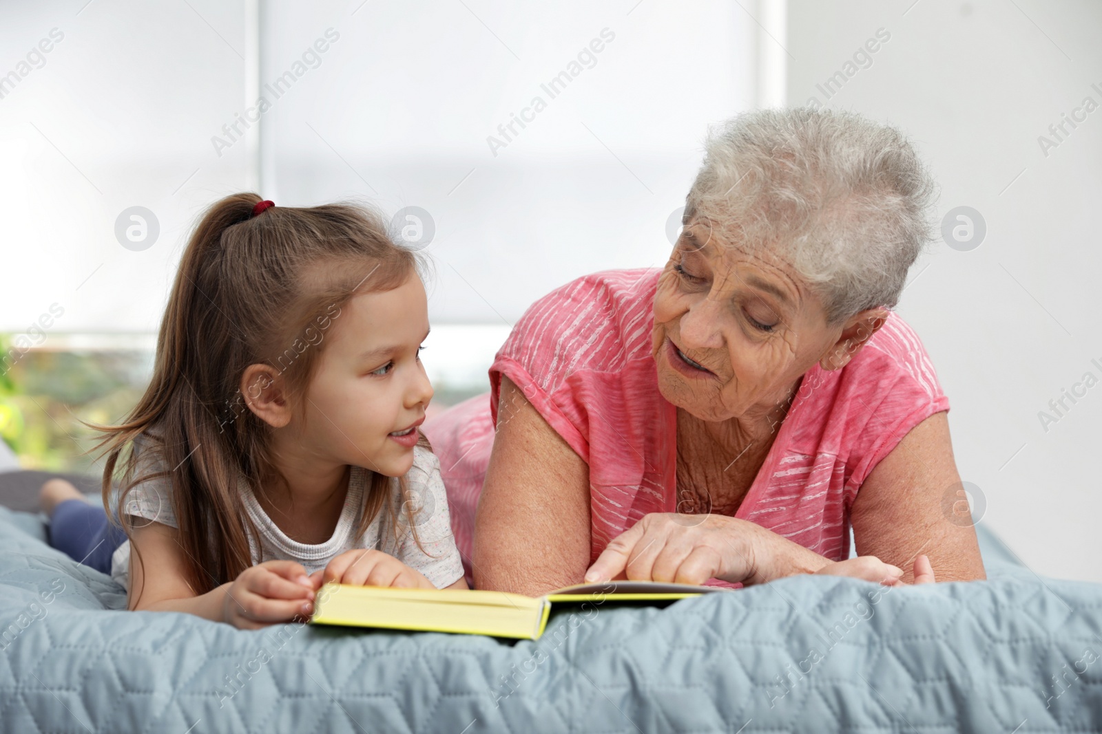 Photo of Cute girl and her grandmother reading book on bed at home