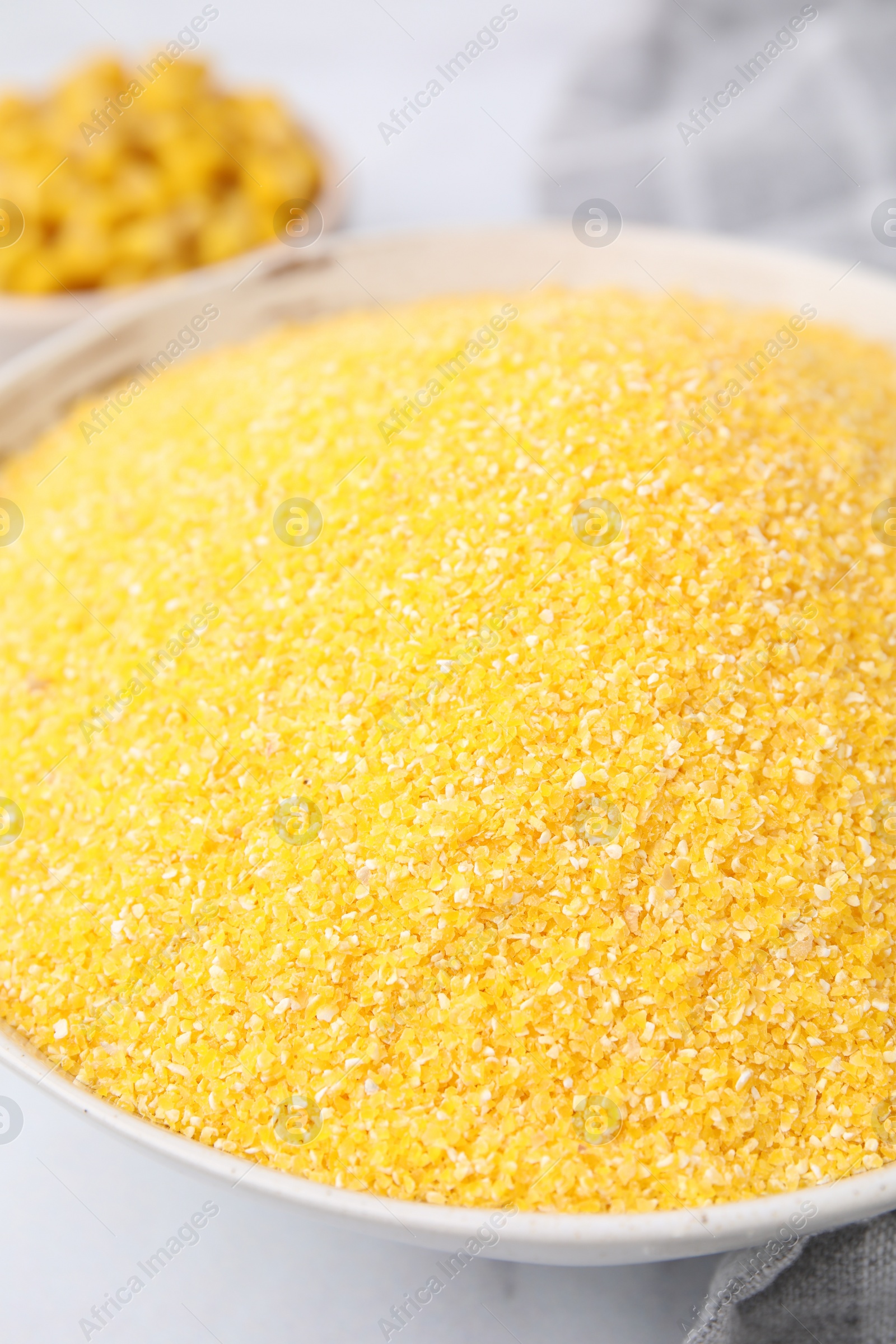 Photo of Raw cornmeal in bowl on white table, closeup