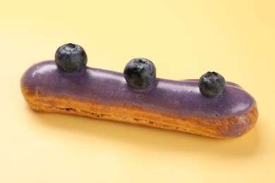 Photo of Delicious purple eclair decorated with blueberries on yellow background