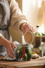 Photo of Woman pickling glass jar of cucumbers at wooden table, closeup