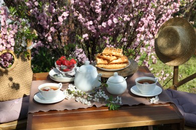 Beautiful spring flowers, freshly baked waffles and ripe strawberries on table served for tea drinking in garden
