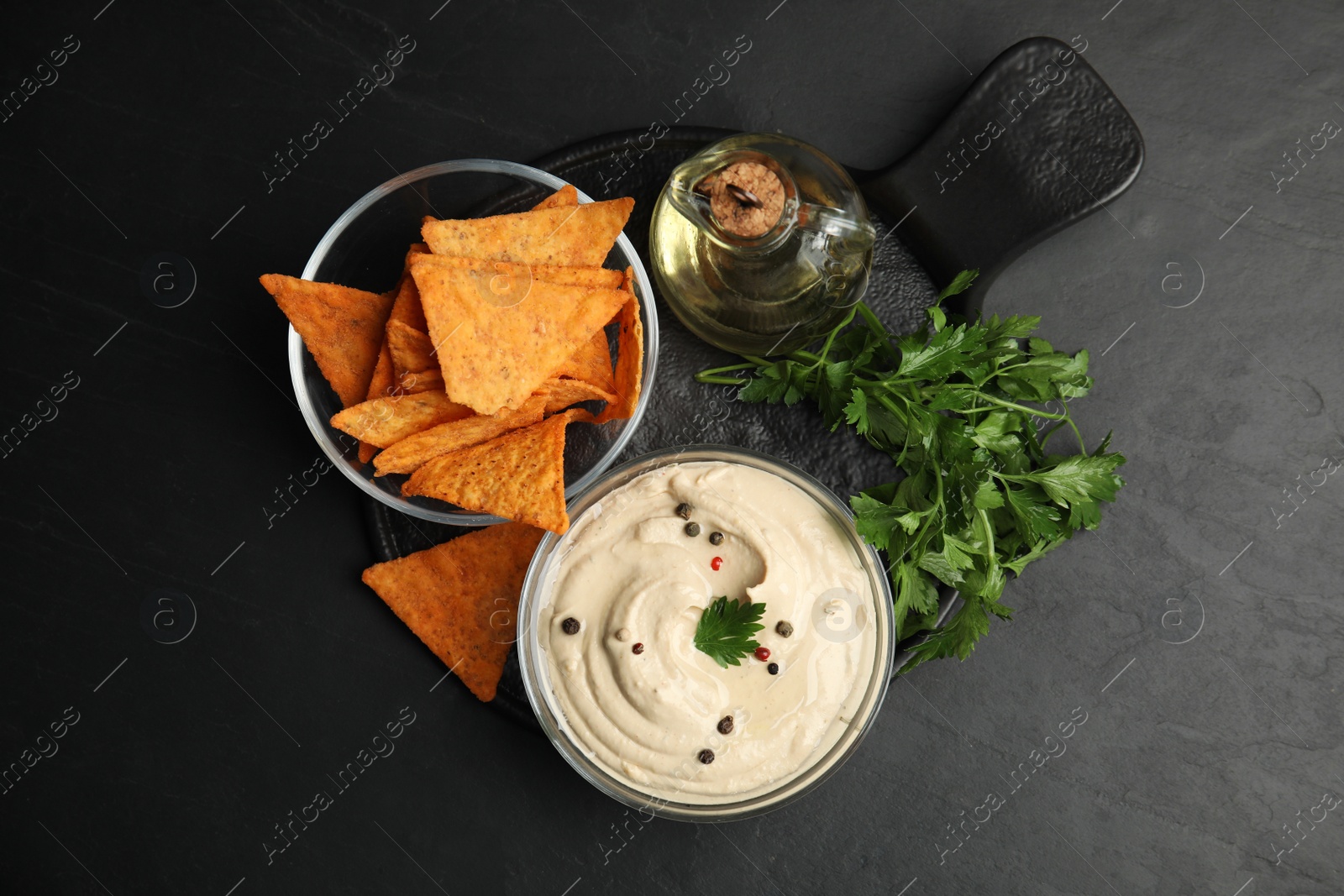 Photo of Delicious hummus with nachos and parsley on black table, top view