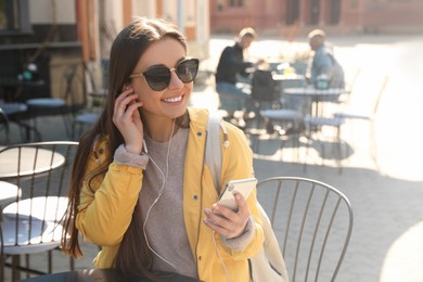Photo of Happy young woman with earphones and mobile phone listening to music in outdoor cafe