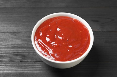 Delicious ketchup in bowl on black wooden table, closeup. Tomato sauce