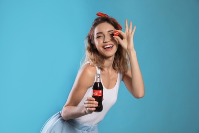 Photo of MYKOLAIV, UKRAINE - NOVEMBER 28, 2018: Young woman with bottle of Coca-Cola and cap on color background