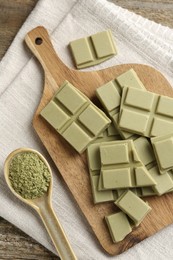Pieces of tasty matcha chocolate bar and powder in spoon on wooden table, top view