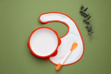 Flat lay composition with baby feeding accessories and bib on green background