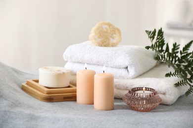 Photo of Spa composition. Burning candles, soap, towels and loofah on soft grey surface