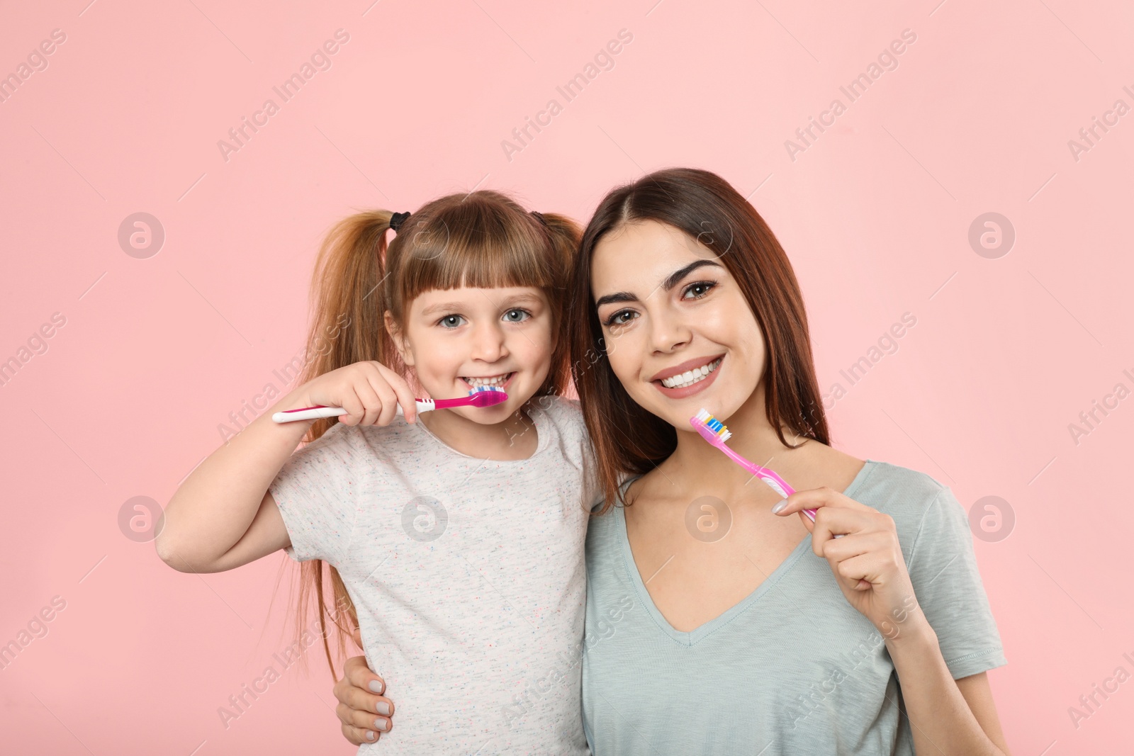 Photo of Little girl and her mother brushing teeth together on color background