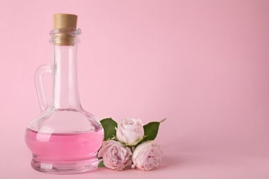 Bottle of essential oil and roses on pink background. Space for text