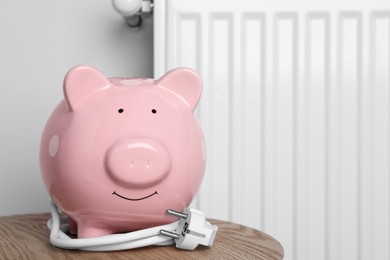 Photo of Piggy bank with plug on wooden table near heating radiator. Space for text