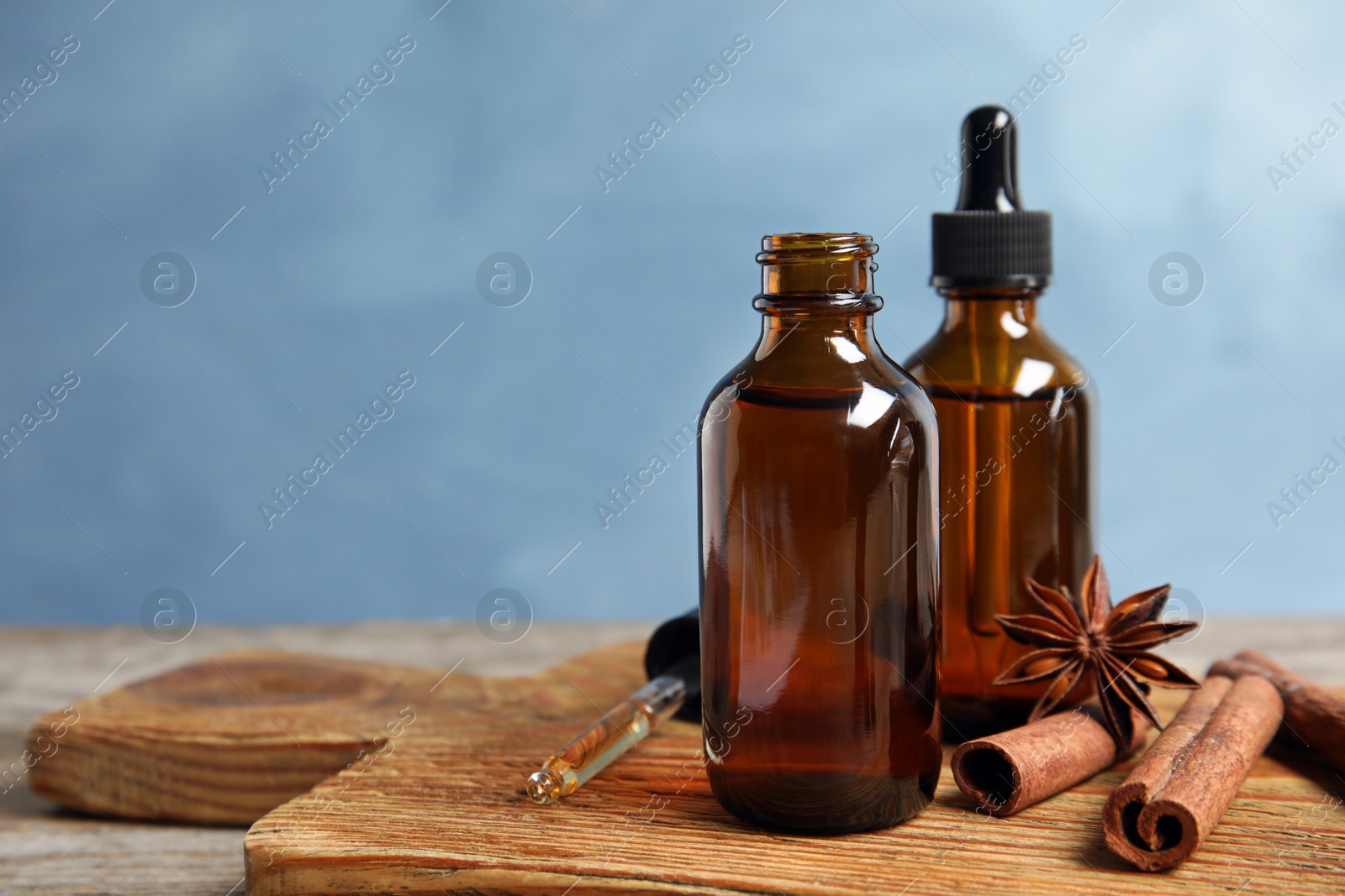 Photo of Bottles of essential oils and cinnamon sticks on wooden table against blue background. Space for text