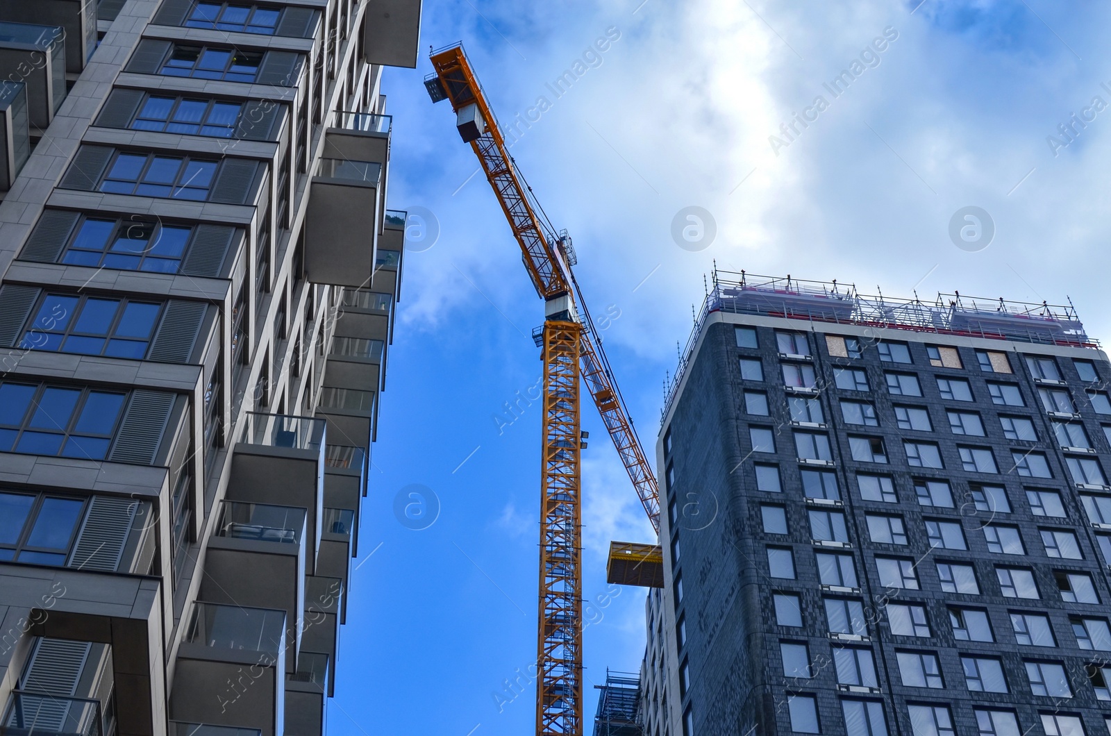 Photo of Exterior of beautiful buildings and construction crane against blue sky, low angle view