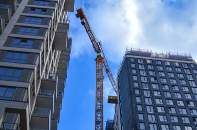 Exterior of beautiful buildings and construction crane against blue sky, low angle view