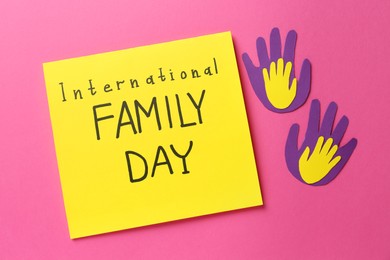 Photo of Paper palms and card with text International Family Day on pink background, flat lay