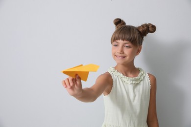 Photo of Cute little girl playing with paper plane on light grey background